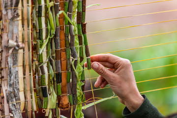 Closeup cropped image of human hand decorating yellow string with green braided leaves and wooden...
