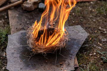 Flame burning using straw as fire starter on grey slate during demonstration of native traditional...