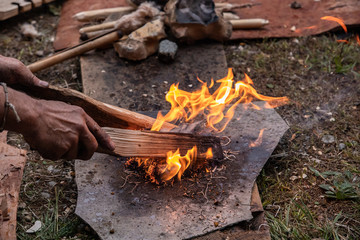 Male hands holding wooden sticks near straw used as fire starter during demonstration of...