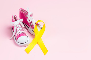 Baby shoes with childhood cancer awareness golden ribbon on pink background with copy space.
