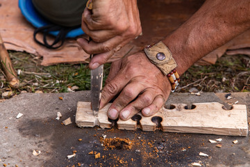 Man hand holding knife while giving demonstration to light fire on wooden slab with burnt holes...