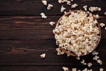 Wooden bowl with salty popcorn on a wooden table. Dark background Selective focus. Flat lay