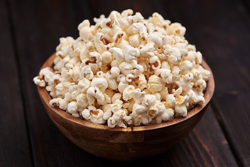 Wooden bowl with salty popcorn on a wooden table. Dark background Selective focus.