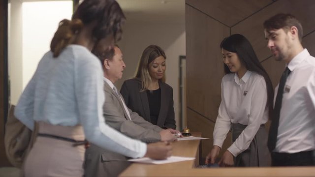 Tracking of hotel receptionists working with clients. Female manager smiling and handing key cards to guests as male administrator giving registration form to black woman booking room
