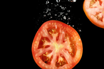 Tomato slices falling into water at black background