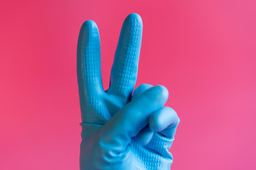 Hand with cleaning glove making peace. Hand in a rubber glove on a pink background