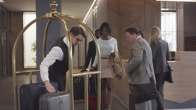Tracking shot of professional bellman in uniform helping guests and putting their suitcases on luggage cart