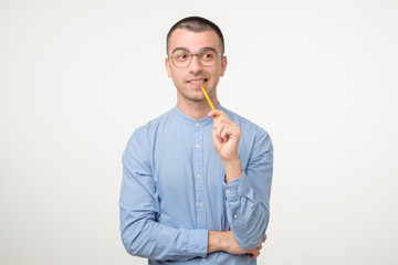 Young hispanic man in glasses is thinking about something with pencil
