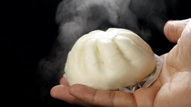 Hot steamed bun on hand with steam in slow motion on black background