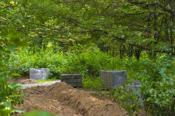 Fototapeta premium A stack of concrete bricks for laying the road in the park. Construction site on a background of green trees.
