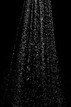 Blurred background with a stream of water splashing out of the shower against a dark background. Image to use as an element or background mock up