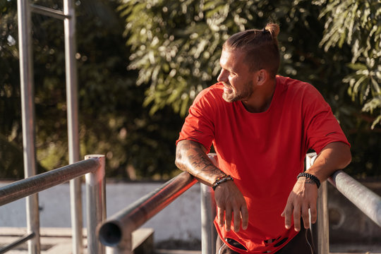Cute young European man in a red T-shirt doing power fitness workout, healthy lifestyle sport concept on parallel bars
