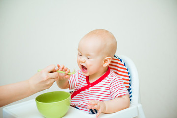 Cute baby eats with spoon sitting in highchair