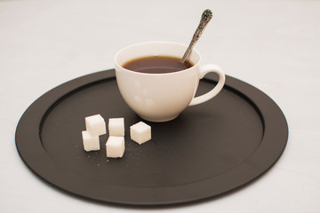 Morning tea in a white cup with sugar cubes on a black tray.