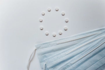a circle figure made of small white tablets and three blue medical masks next to it on a light blue-gray background