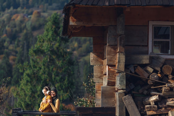 Obraz premium mother and her baby are enjoying early fall. Young mother with daughter outside on terrace near log house in forest.