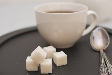 Morning tea in a white cup with sugar cubes on a black tray.