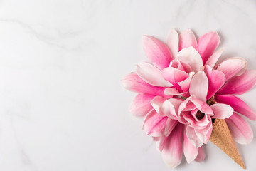 Creative layout made with pink magnolia flowers in ice cream cone on white marble background. Flat lay. top view