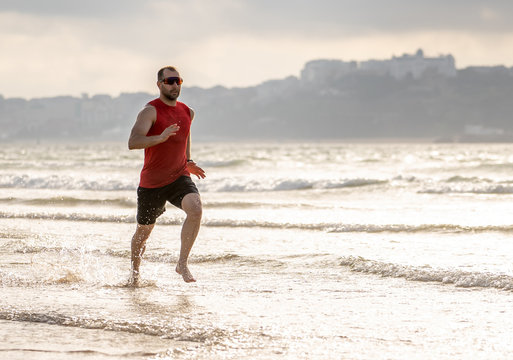 Fitness athlete runner man running barefoot on the beach sand by the sea water