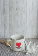 Morning coffee in a white mug with a red heart and ceramic figurine
