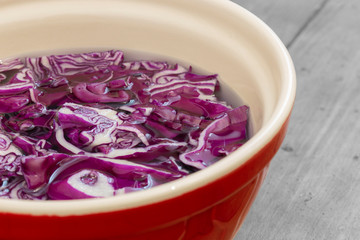 Sliced red cabbage soaking in water in a ceramic bowl.  With a grey wood background.