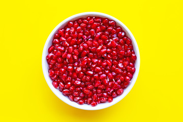 Pomegranate seed in white bowl on yellow background.