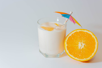 A glass of yogurt with a multi-colored umbrella and slices of orange near a sliced orange