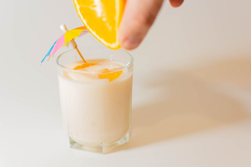 Squeeze juice from an orange into a glass of yogurt with a multi-colored umbrella and slices of orange next to the chopped orange