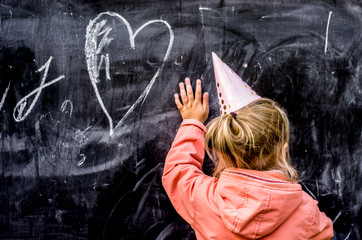 Girl in a holiday cap draws a heart with chalk.