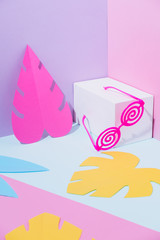 Summer party composition on a geometric background with pink plastic twisted sunglasses and tropical palm leaves. Beach or swimming pool concept