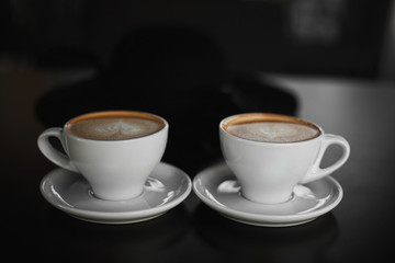 Two white cups of Cappuccino coffee with heart-shaped milk foam. Side view on two cups of latte coffee with heart figure on milk foam on black background. Lifestyle