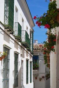 View down old town street with geraniums in pots on walls, Arcos de la Frontera, Spain.