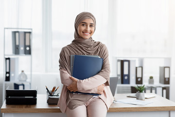 Smiling Arabic Businesswoman Holding Folders And Posing Near Workplace In Office