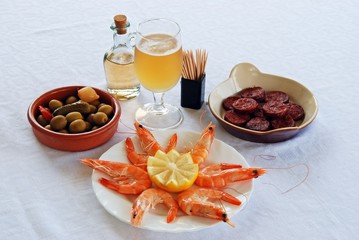 A selection of tapas with beer, King prawns with lemon, Sliced Chorizo sausage, and green olive cocktail, Spain.