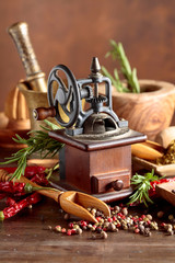 Vintage pepper mill with kitchen utensils, spices and rosemary on a old wooden table.