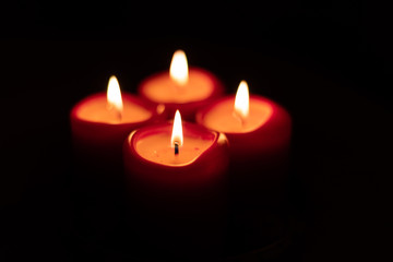 Xmas Christmas season symbol. Four candles symbolize advent weeks. Detail of four red candles burning, isolated with black surrounding.