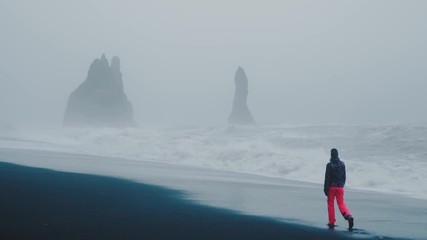 A young woman walking alone along a beach in Iceland. - Powered by Adobe