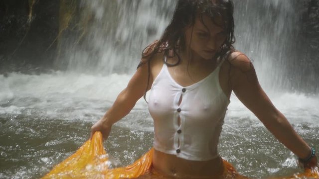 A closeup shot of a young woman, dancing in the water with a yellow piece of fabric in slow motion. Looking at the camera with an intense and serious look.