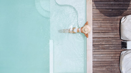 Woman in straw hat relaxing in clear pool water in hot sunny day on Bali villa