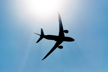 Silhouette of an airplane flying in the sky under the sun.