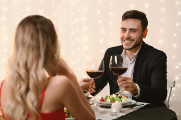 Romantic couple clinking wine glasses during Valentine Day dinner in restaurant