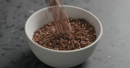 closeup flaxseed falling into white bowl on terrazzo countertop