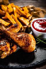 Roast chicken drumsticks with french fries on black stone board
