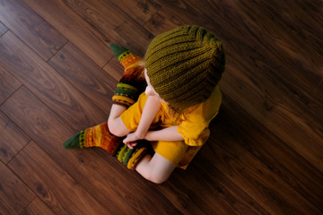 In the village, a little girl in bright multi-colored knitted socks and a knitted hat sits on a...