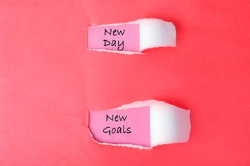 Success motivation concept. In a red sheet of paper, two holes are broken, in which there are inscriptions: "New day. New goals.".