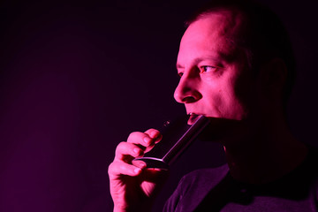 A closeup of a man drinking alcohol straight from the aluminum bottle, with pink neon light, vibrant color and dark background.