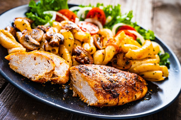 Roast chicken breast with pasta and vegetables on wooden background