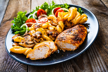 Roast chicken breast with pasta and vegetables on wooden background