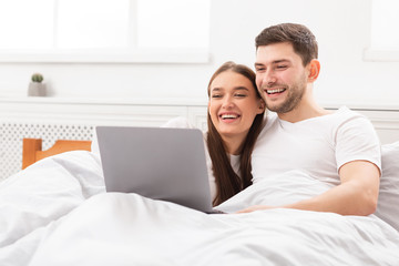 Couple Watching Movie On Laptop Lying In Bed At Home