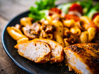 Roast chicken breast with pasta and vegetables on wooden background